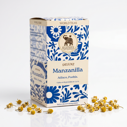 Caja de Manzanilla Deluxe Haathee con 16 sachets piramidales, acompañada de flores de manzanilla.
